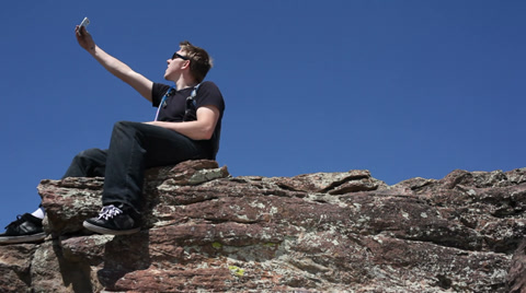 Young Man On Cliff Taking Photo Of Himself