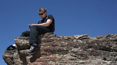 Young Man Using Mobile Phone On Cliff