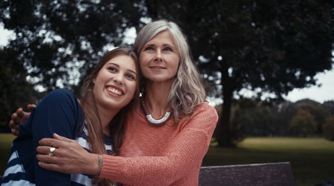 Mother And Daughter Sit In Park Together And Share A Hug